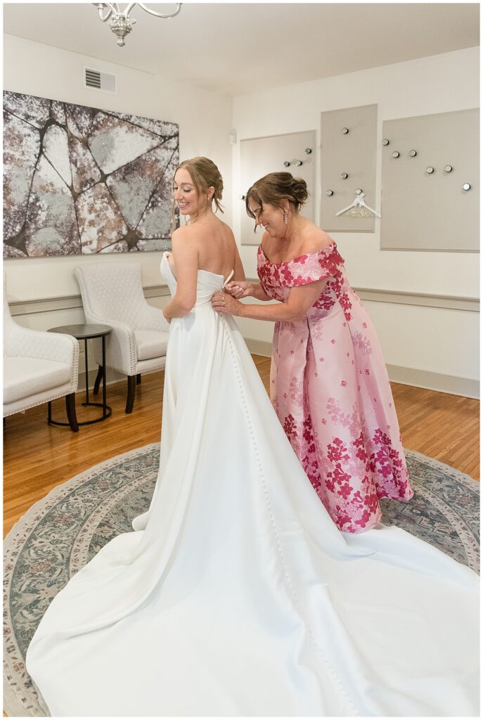 bride's mother buttoning up the back of bride's white wedding gown at this Barn at Silverstone Pink and Black Wedding
