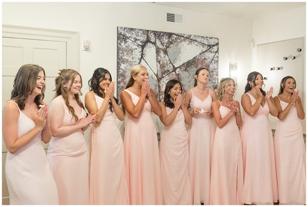nine bridesmaids in light pink gowns gasping as they see bride in bridal sweet for this Barn at Silverstone Pink and Black Wedding