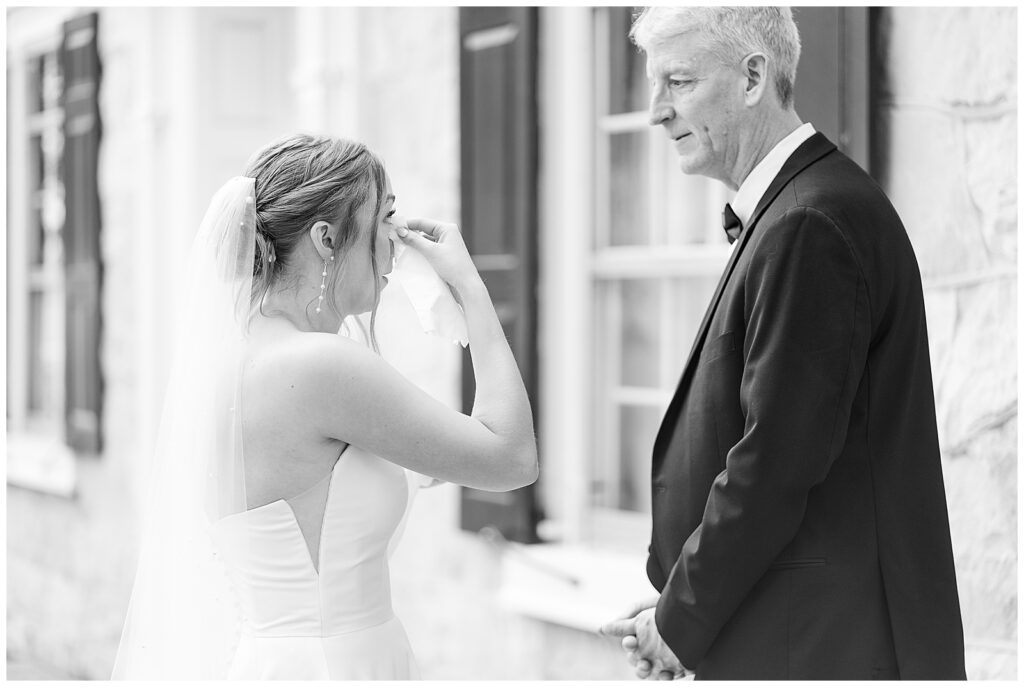black and white photo of bride wiping her eyes during first look moment with her dad at this Barn at Silverstone Pink and Black Wedding