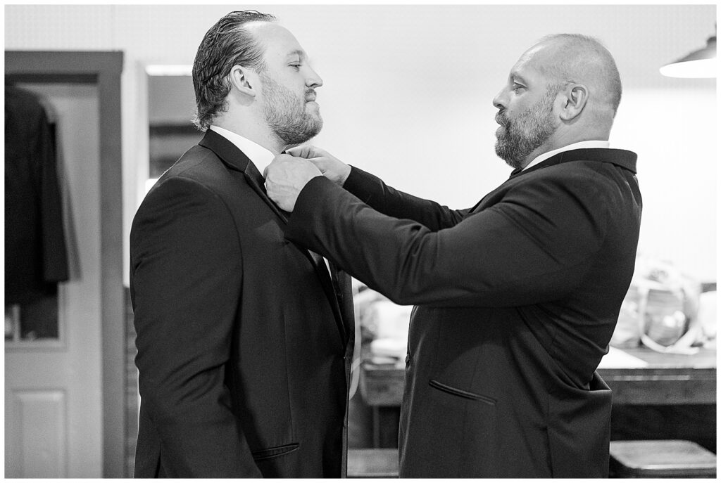 best man adjusting groom's bowtie for his black suit for this Barn at Silverstone Pink and Black Wedding