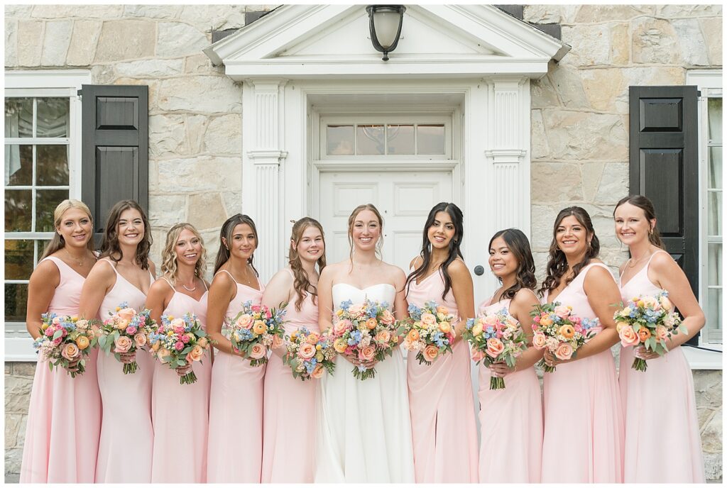 bride surrounded by her bridesmaids by the front door of the stone house at this Barn at Silverstone Pink and Black Wedding
