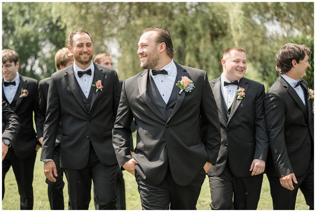 groom looking right and walking towards camera with his hand in pocket with groomsmen for this Barn at Silverstone Pink and Black Wedding