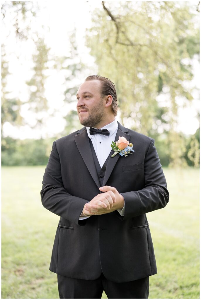 groom clasping hands and looking right in black tux with pink rose boutonniere in lancaster county