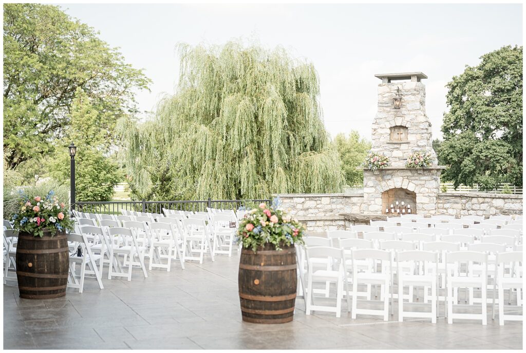 rows of white chairs facing outdoor stone fireplace and chimney with barrel of flowers for outdoor wedding ceremony in lancaster pennsylvania