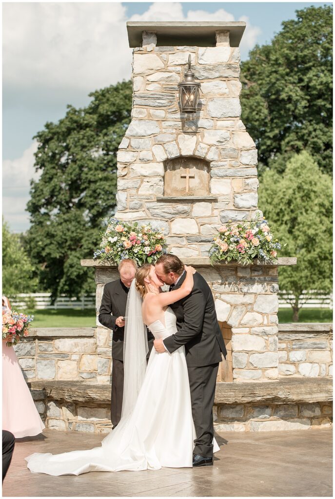 couple kissing during wedding ceremony with stone fireplace behind them at the barn at silverstone