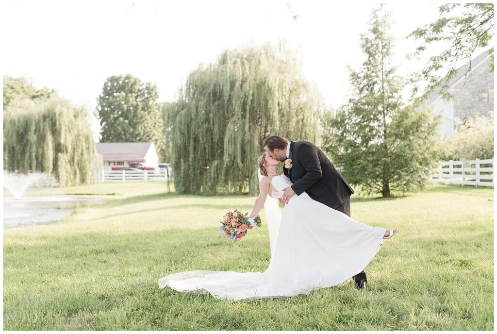 groom dipping his bride back as they kiss by willow tree on sunny summer day in lancaster county