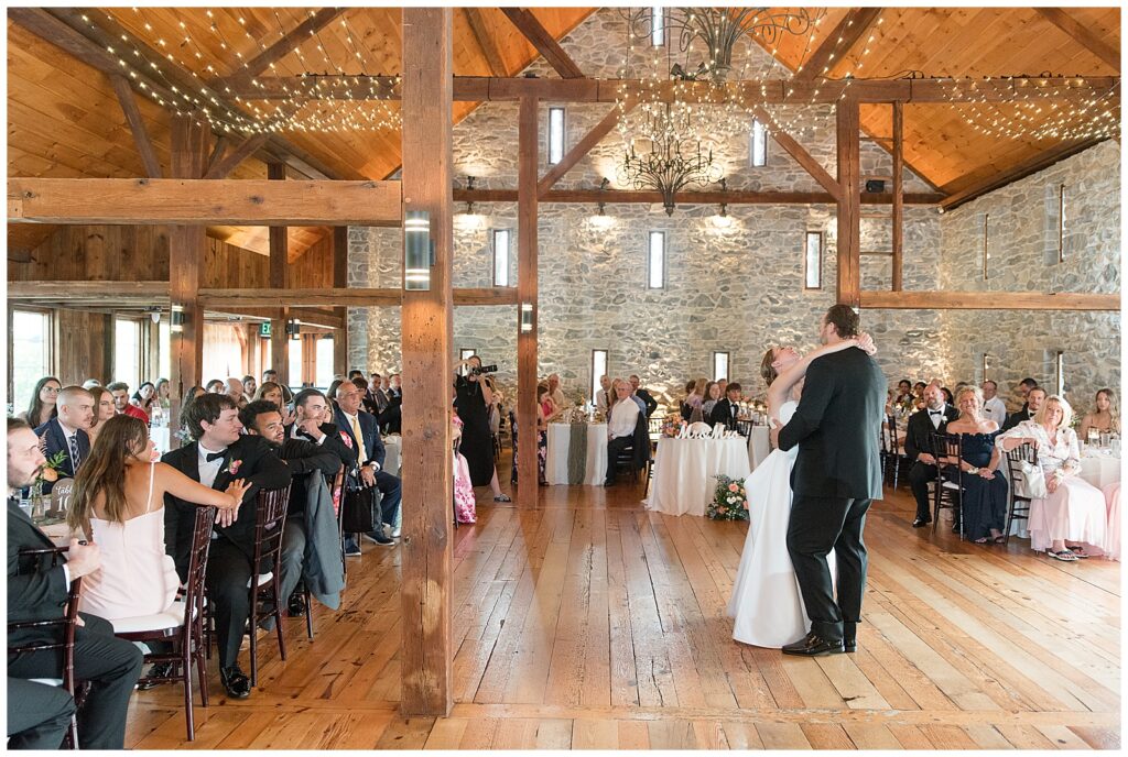 couple sharing their first dance as guests watch during indoor barn reception at this Barn at Silverstone Pink and Black Wedding