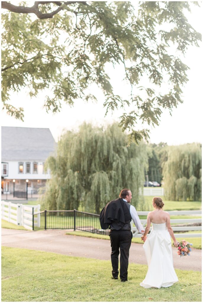 couple holding hands and walking away from camera toward white stone barn for this Barn at Silverstone Pink and Black Wedding