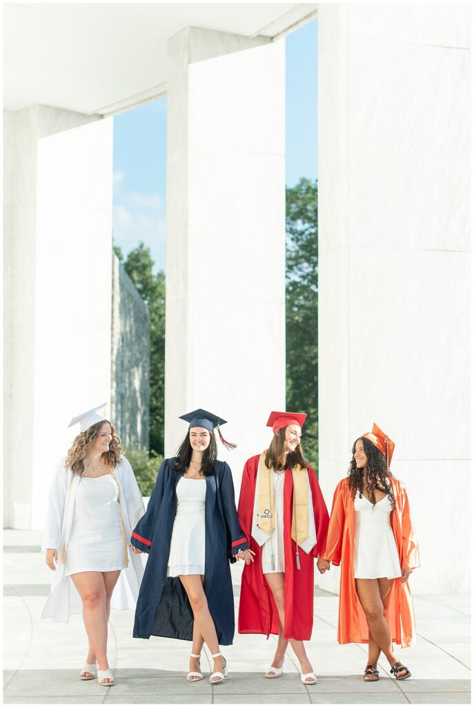 four senior girls in their colorful high school caps and gowns for graduation by white columns for this Founders Hall Cap and Gown Session