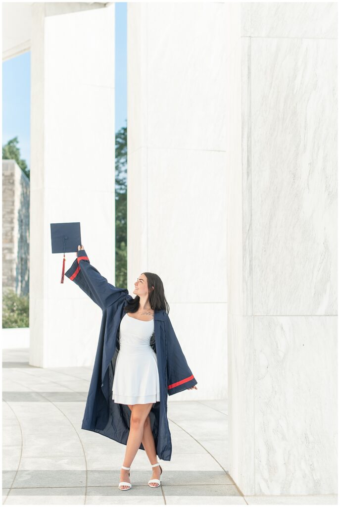 senior girl in navy blue graduation gown raising her cap high with her right hand for this Founders Hall Cap and Gown Session