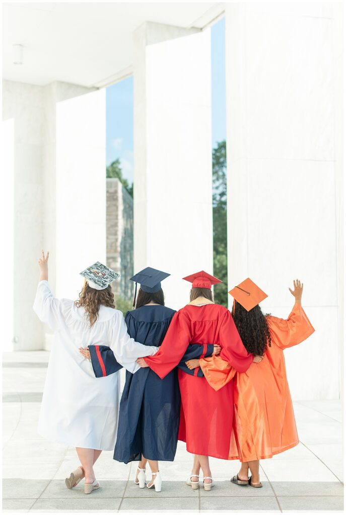 four senior girls in caps and gowns hugging with their backs toward the camera at this Founders Hall Cap and Gown Session