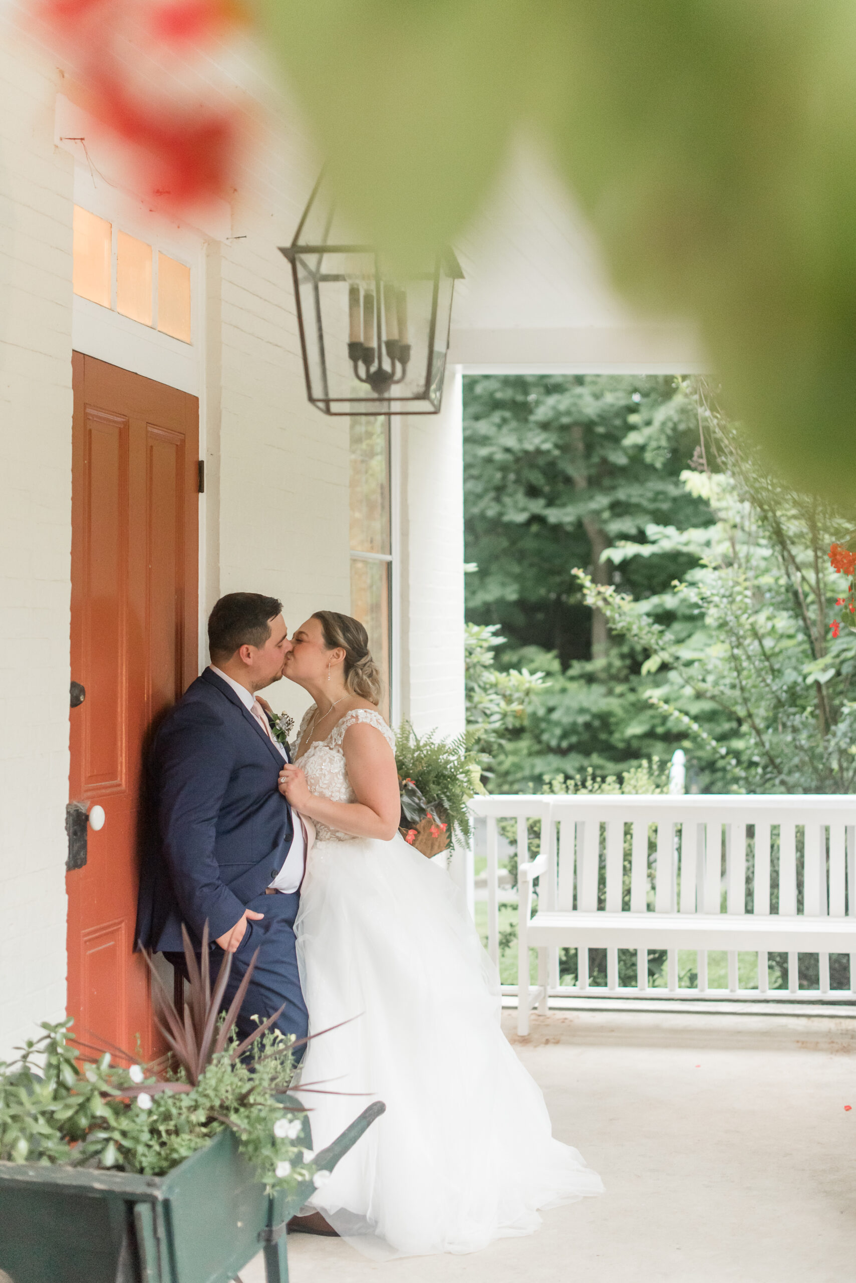 couple kissing by orange house door on front porch at riverdale manor wedding