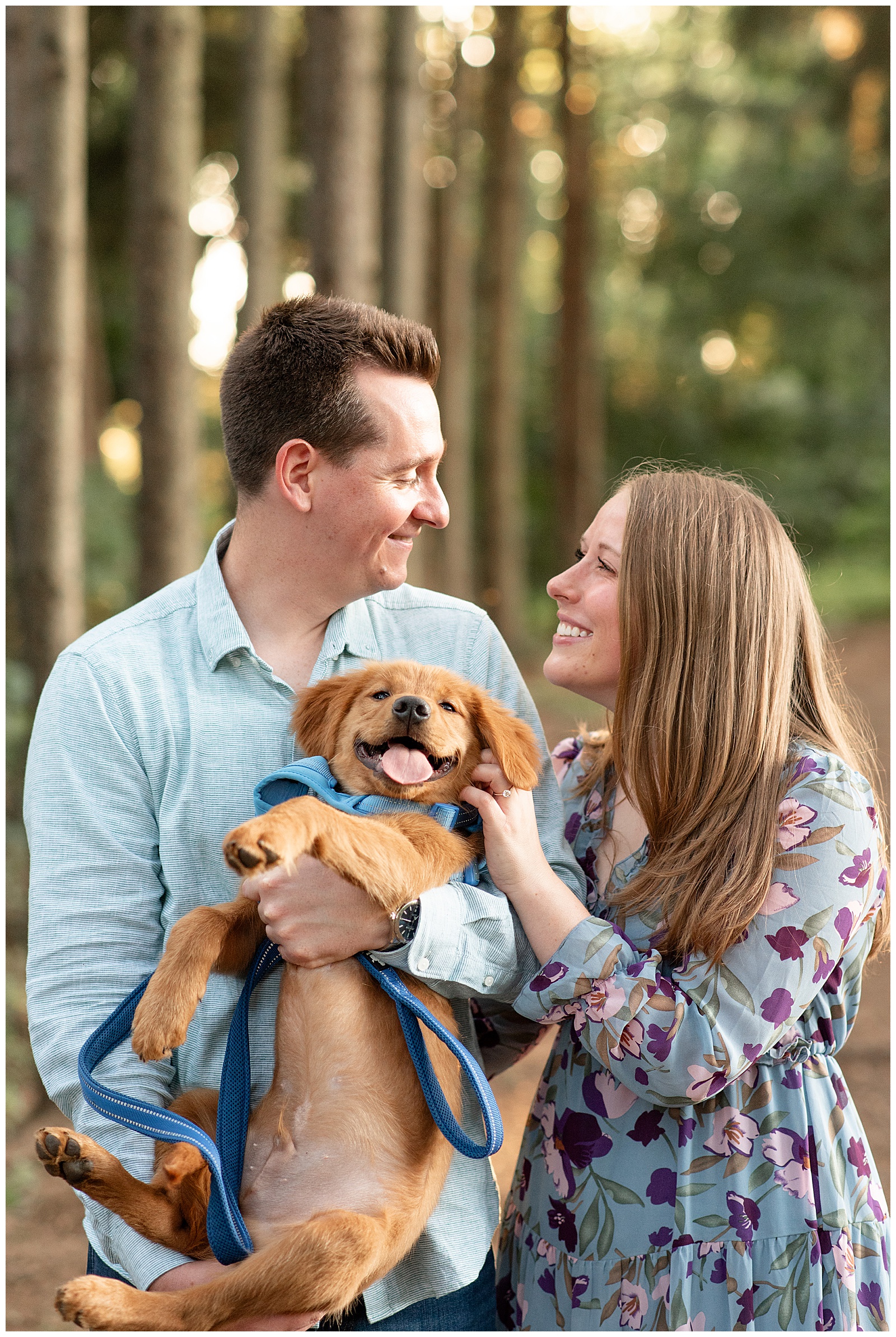couple smiling while guy holds golden retriever pup for this Puppy-Loving Overlook Park Engagement Session