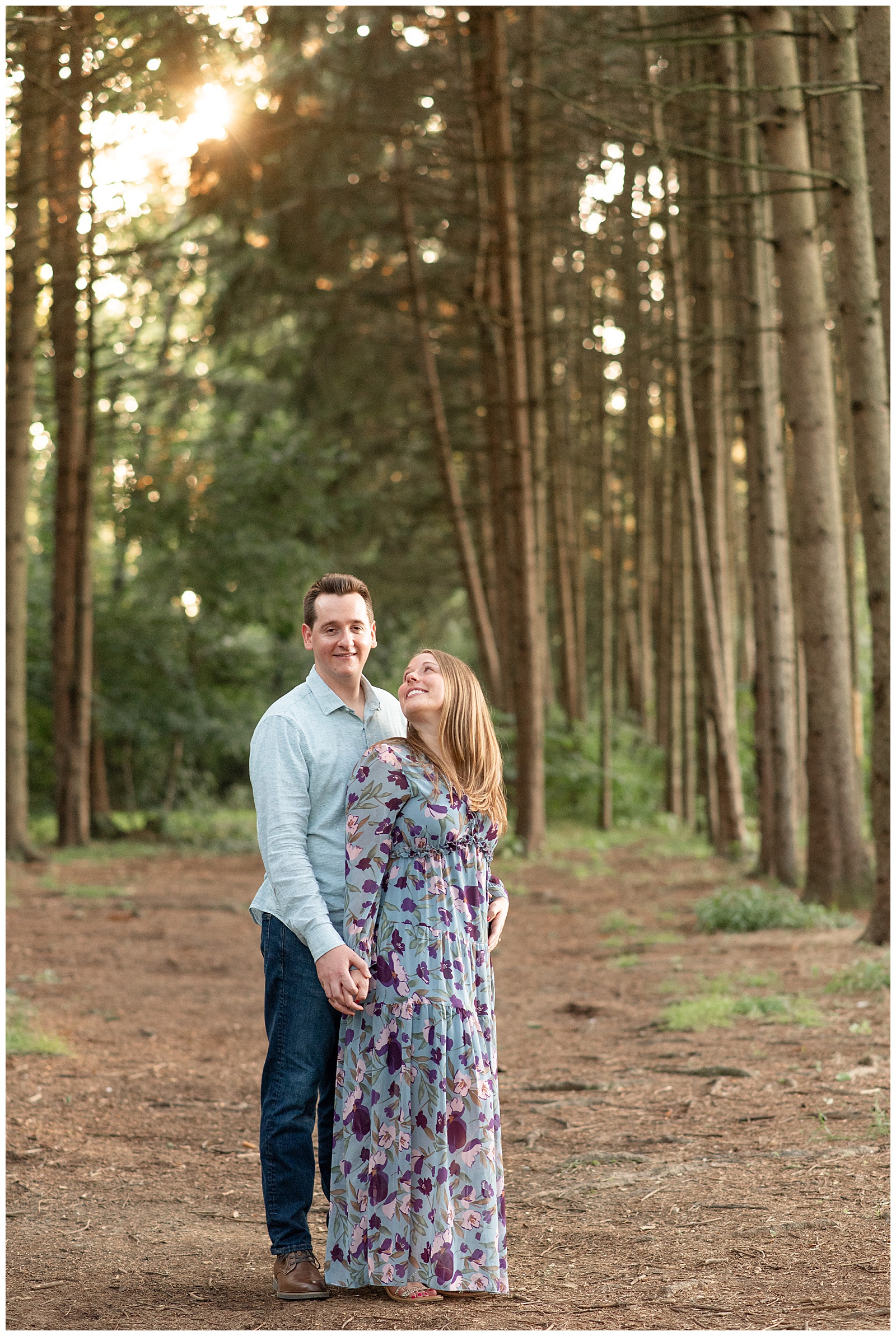 bride looking back at her soon-to-be groom as they hold hands by evergreen trees for this Puppy-Loving Overlook Park Engagement Session