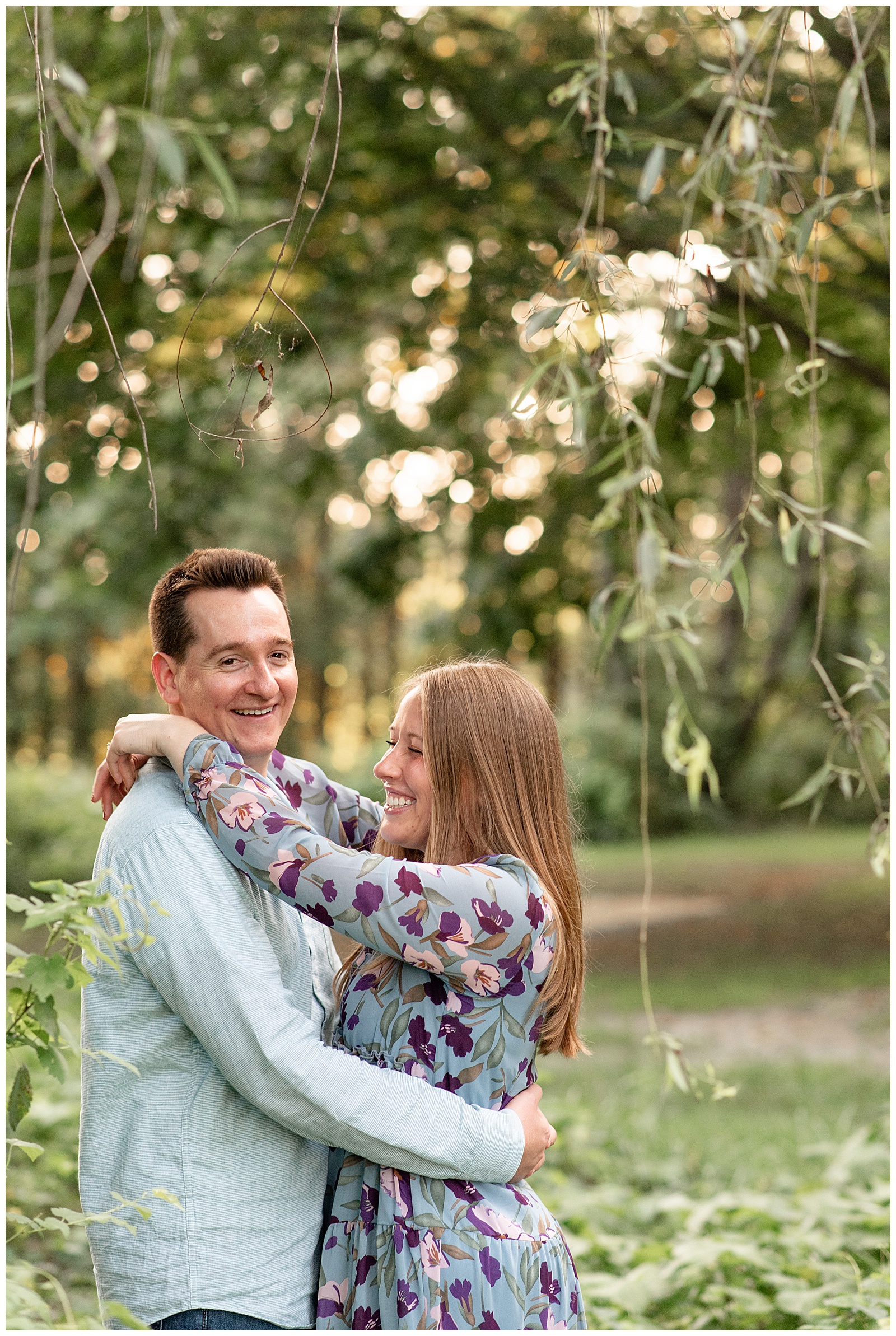 couple hugging while standing under tree at sunset for this Puppy-Loving Overlook Park Engagement Session