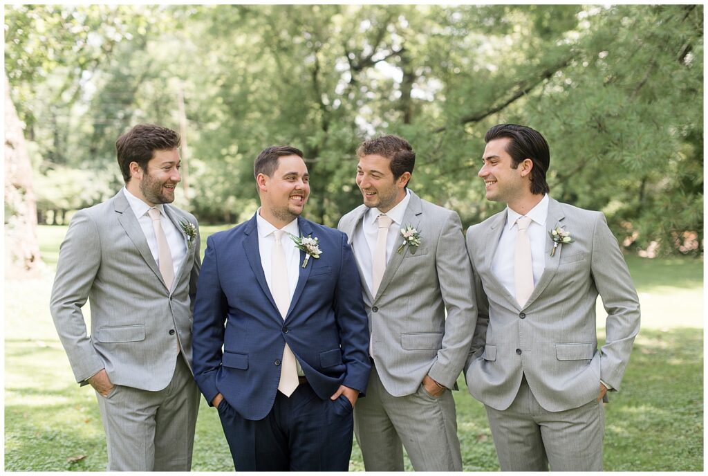 groomsmen photo of them looking at the groom. Groomsmen wearing light gray suits and the groom wearing navy