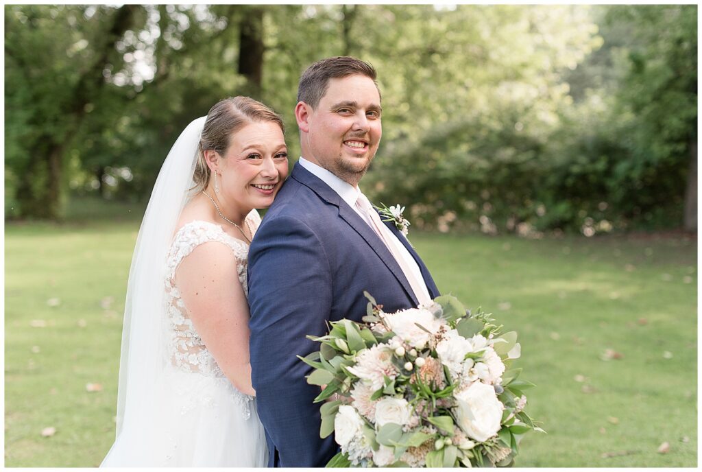 bride and groom smiling to camera with bride hugging him from behind