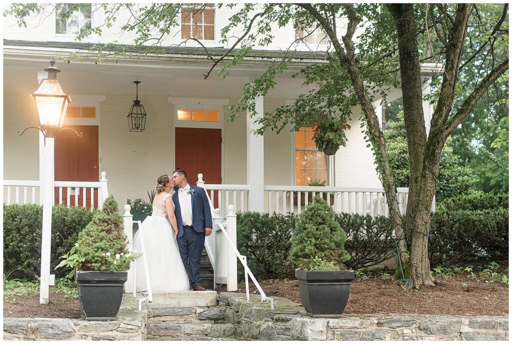 bride and groom holding hands and sharing kiss at steps of farmhouse at Riverdale Manor