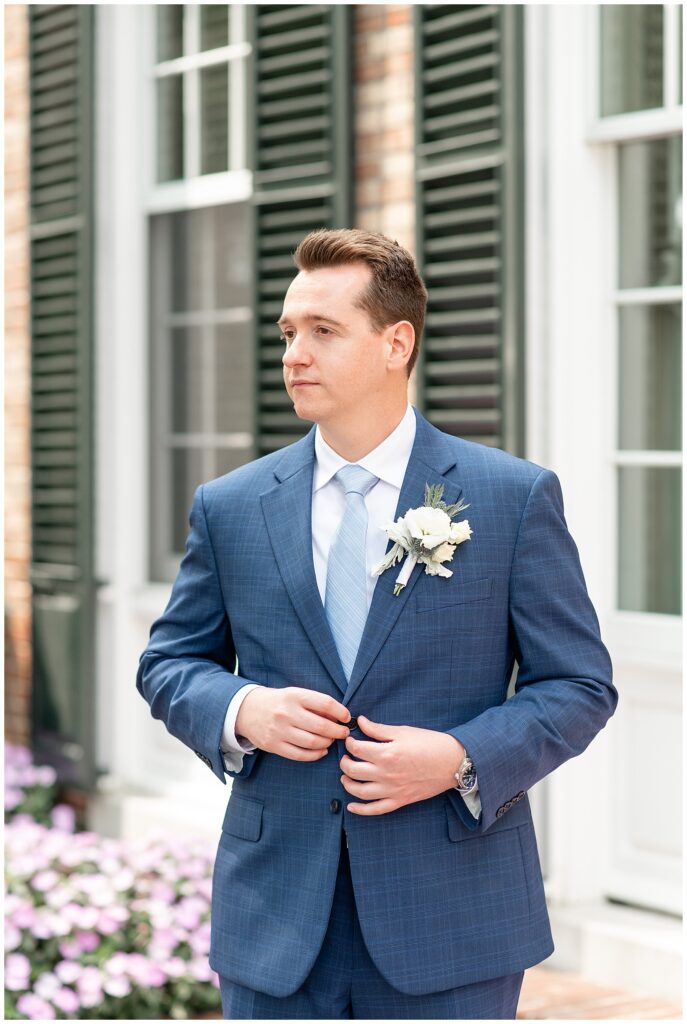 groom buttoning up his navy blue suit coat by house for this Drumore Estate Summer Wedding