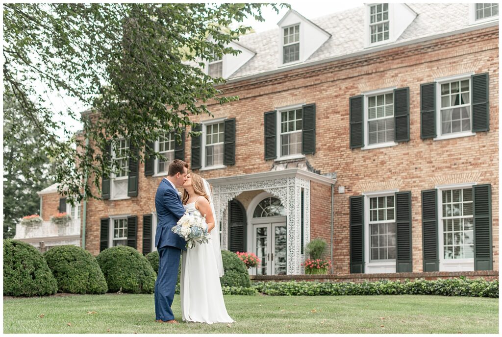 couple kissing in front of beautiful brick home for this summer Drumore Estate Summer Wedding
