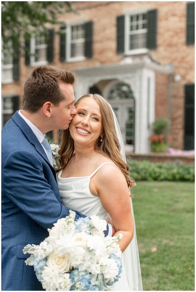 groom kissing his bride on her right cheek as she smiles at this Drumore Estate Summer Wedding