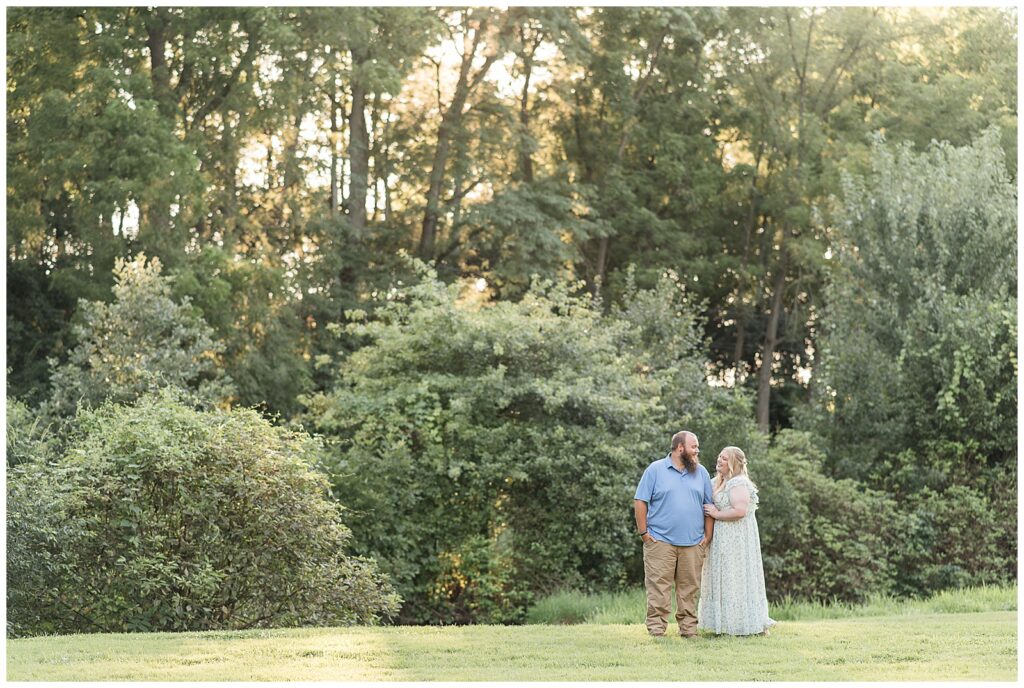 couple standing close and smiling at each other by trees at this Historic Poole Forge Summer Engagement Session