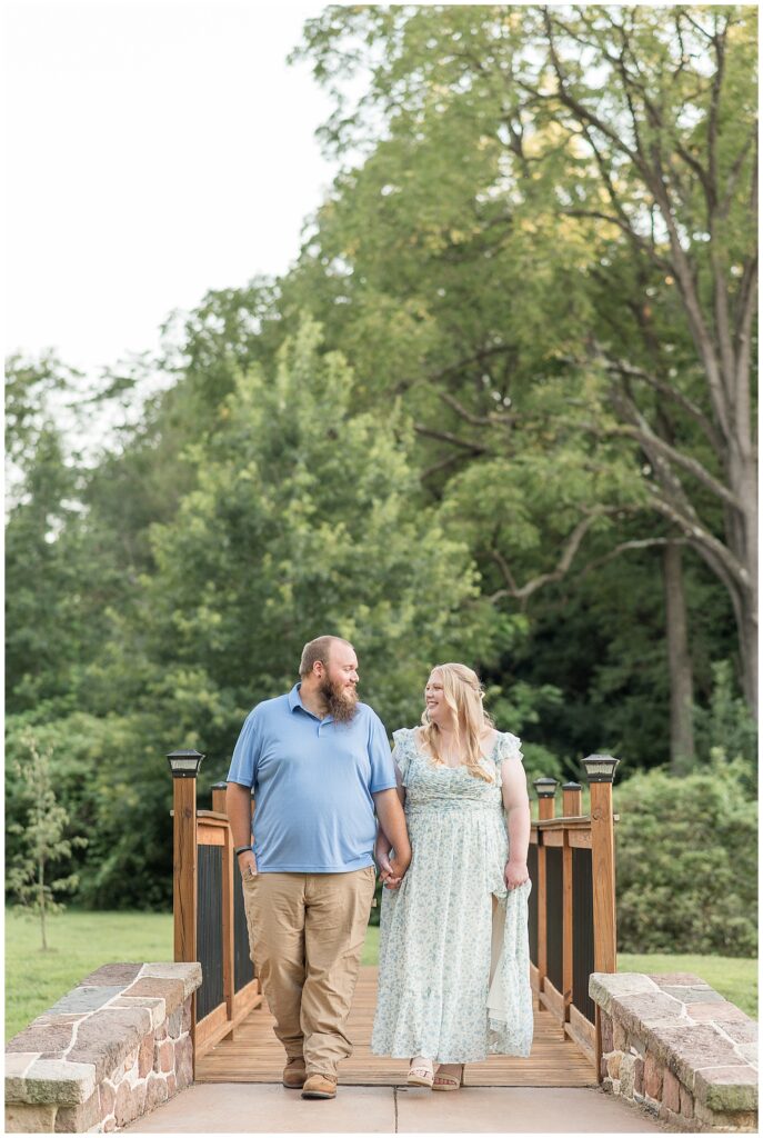 couple holding hands as they walk over wooden bridge at this Historic Poole Forge Summer Engagement Session