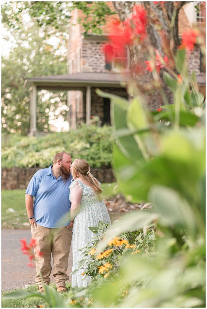 couple kissing with stone house in background for this Historic Poole Forge Summer Engagement Session