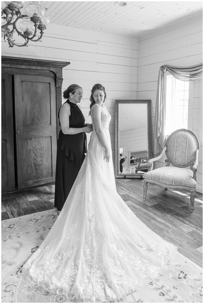 black and white photo of bride with her mom zipping up her white wedding gown in bridal suite for this Lakeview Farms Summer Wedding