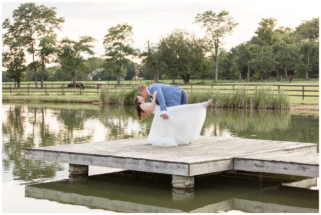 groom dipping back his bride as they kiss on dock of lake for this Lakeview Farms Summer Wedding