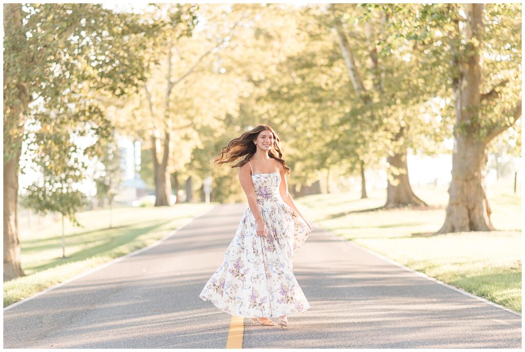 senior girl in floral dress spinning in middle of road for this Summer Masonic Village Senior Session