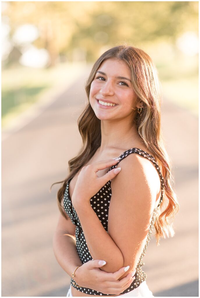 senior girl in black tank top with white polka dots with left shoulder towards camera for this Summer Masonic Village Senior Session