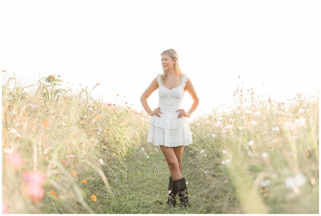 senior girl in white dress and cowboy boots with hands on hips for this Summer Wildflower Field Senior Session
