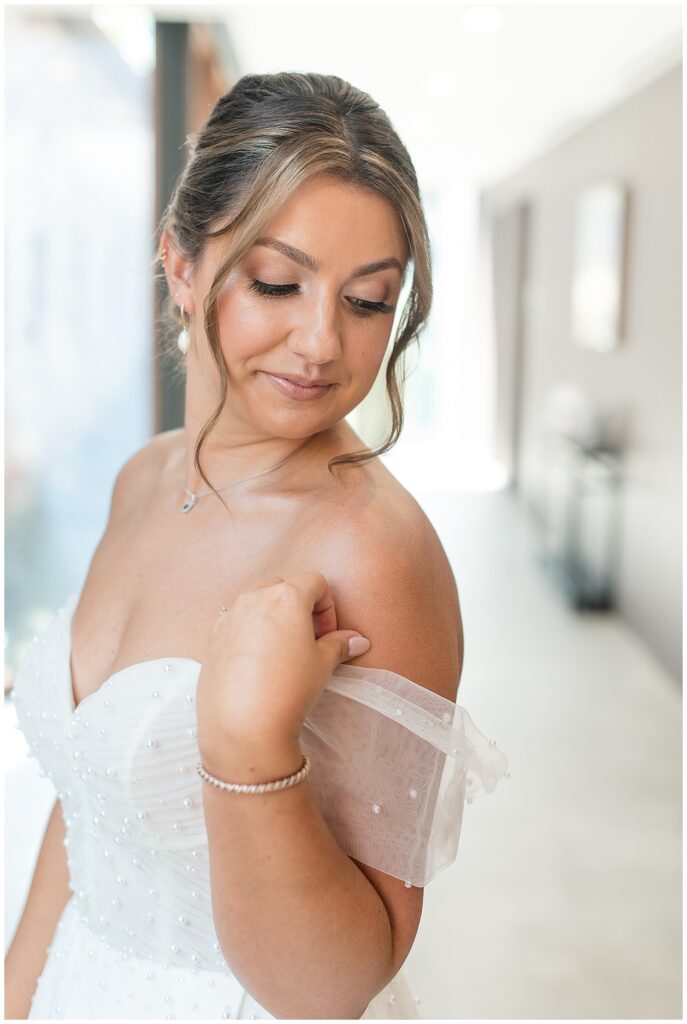 bride with off the shoulder white wedding grown with pearl details looking down at left shoulder for this Elizabeth Furnace Fall Wedding