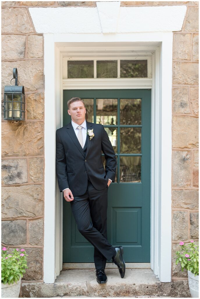 groom in black suit leaning against doorway by dark green door for this Elizabeth Furnace Fall Wedding