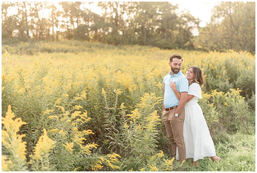 woman hugging man from behind in field of yellow flowers for this Fall Hibernia Park Engagement Session
