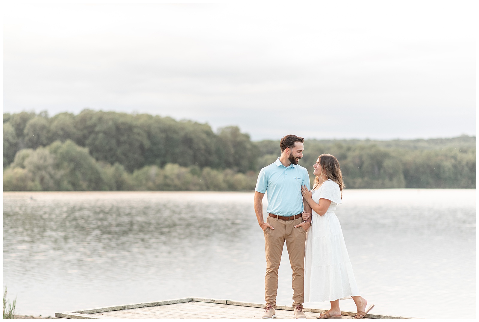 woman holding onto man's left arm on dock by lake for this fall Fall Hibernia Park Engagement Session