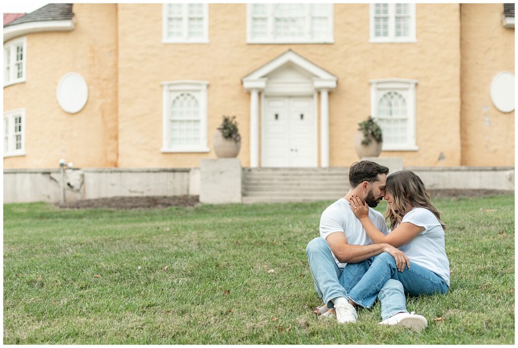 couple sitting together on lawn in front of peach-colored home for this Fall Hibernia Park Engagement Session