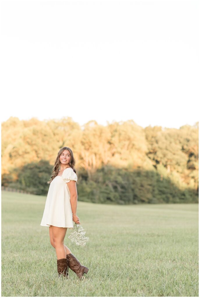 senior girl in white dress and cowboy boots holding bouquet behind her back at this Hibernia Park Senior Session