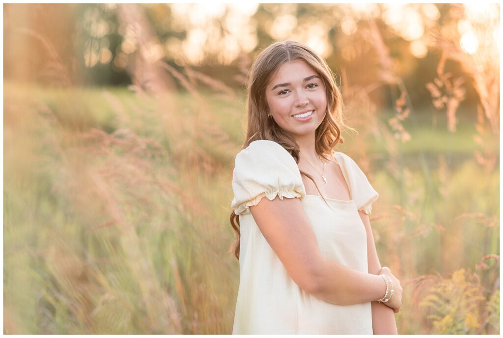 senior girl holding left elbow with right hand by tall wild grasses for this Hibernia Park Senior Session