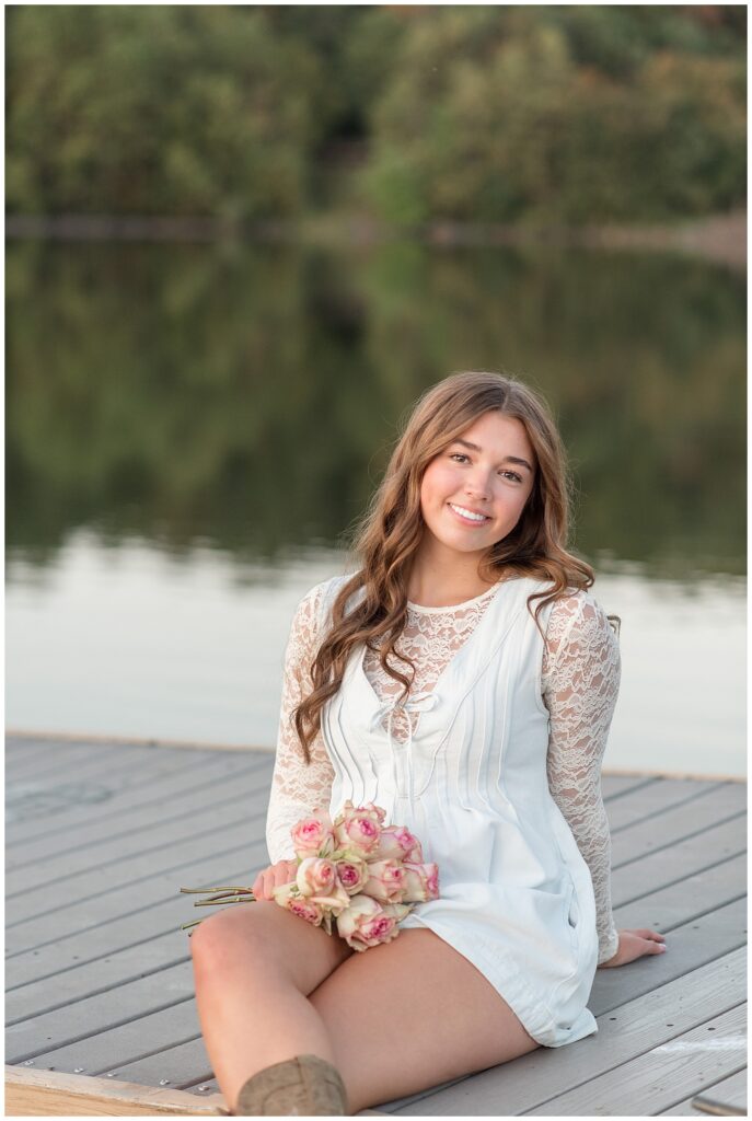 senior girl sitting on dock by lake with flowers in her lap for this Hibernia Park Senior Session