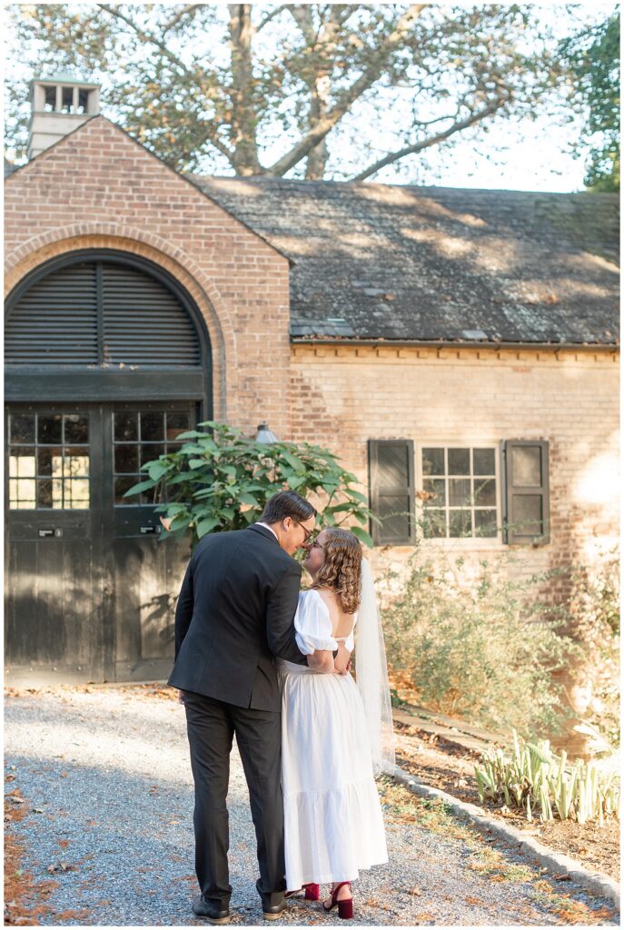 couple kissing with their backs toward camera by brick building for this Conestoga House and Gardens Engagement Session