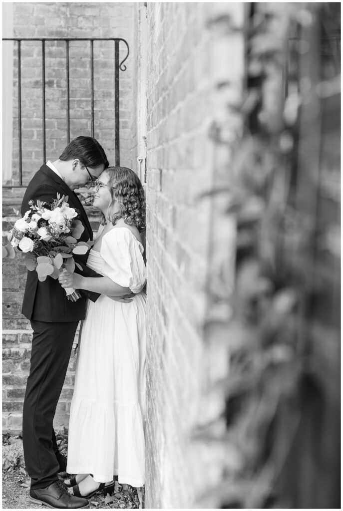 black and white photo of couple standing close and touching foreheads by brick wall for this Conestoga House and Gardens Engagement Session