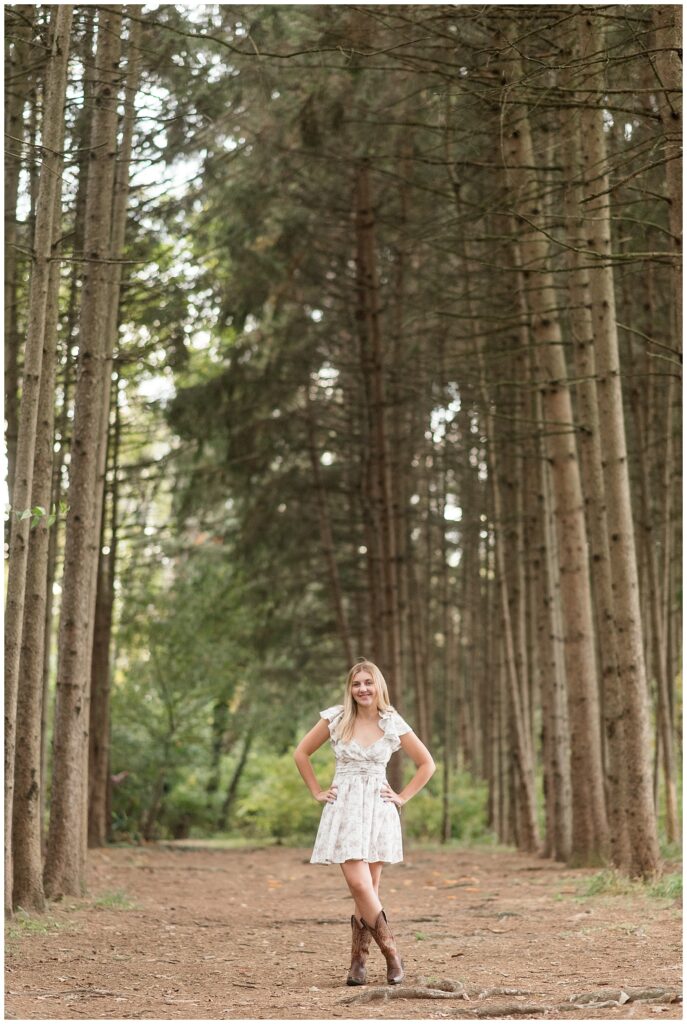 senior girl with hands on hips wearing white floral dress and cowboy boots for this Fall Overlook Park Senior Session