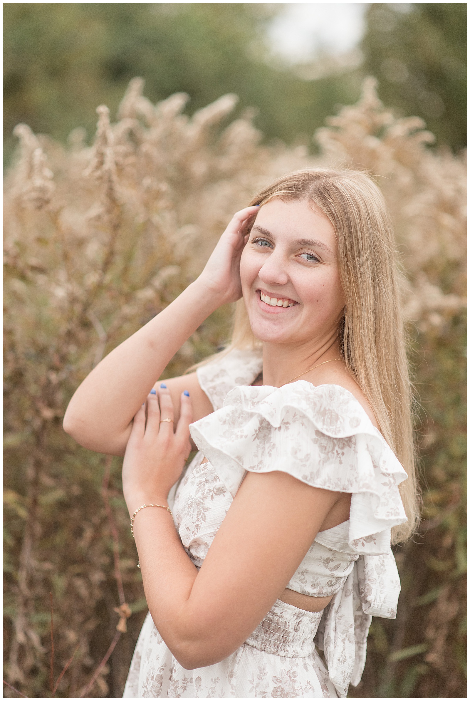 senior girl tucking hair behind her ear with her right hand by dried flowers for this Fall Overlook Park Senior Session