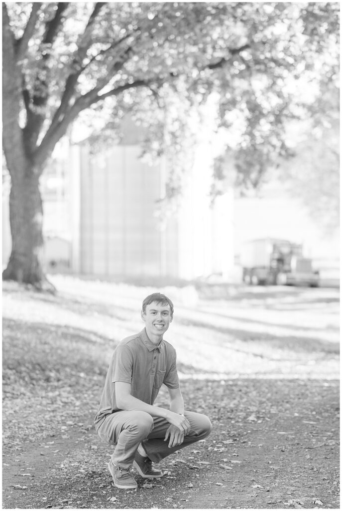 black and white photo of senior guy crouched down with grain bin in background for this Family Farm Senior Guy Session in Lancaster County