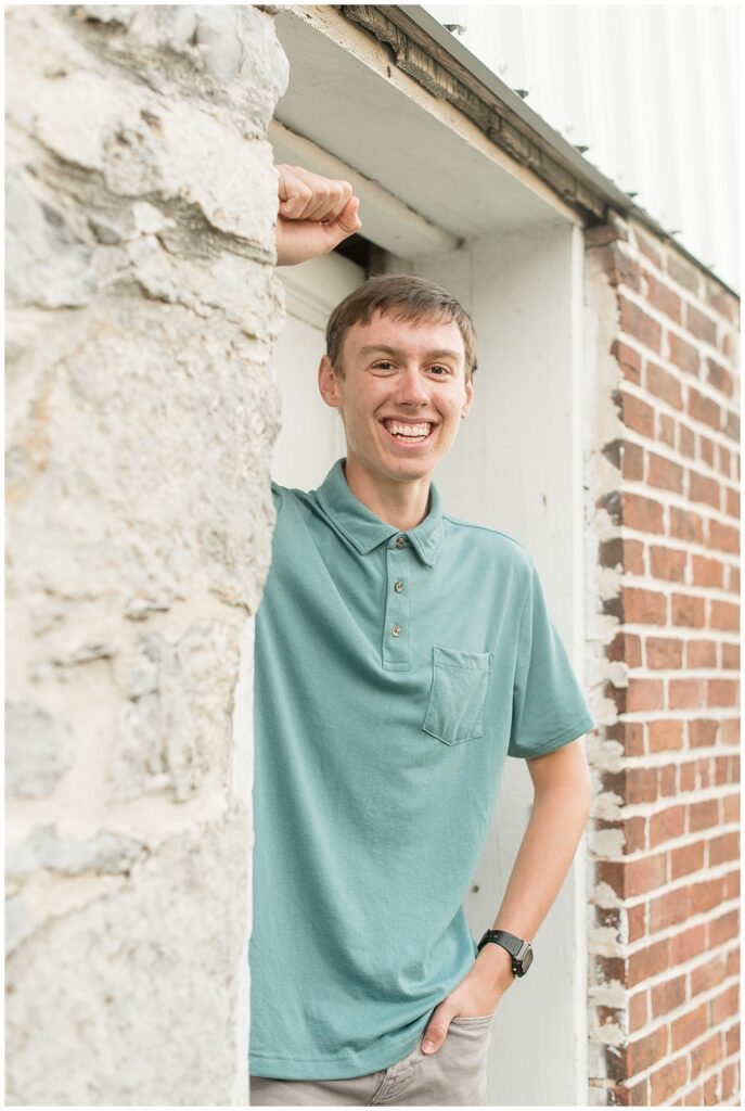 senior guy leaning against door frame of historic building for thi sFamily Farm Senior Guy Session in Lancaster County