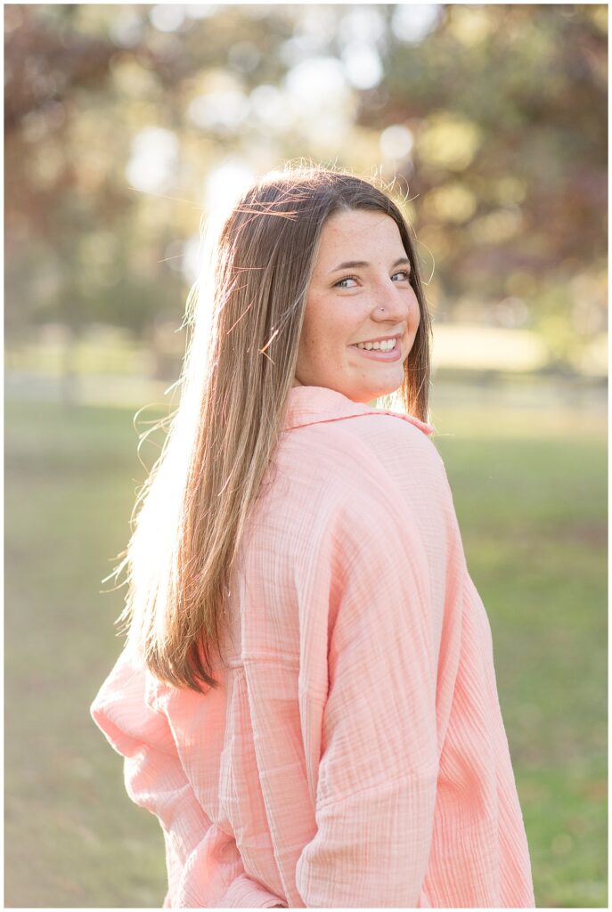 senior girl looking back over right shoulder wearing light pink shirt for this Longs Park Fall Senior Session