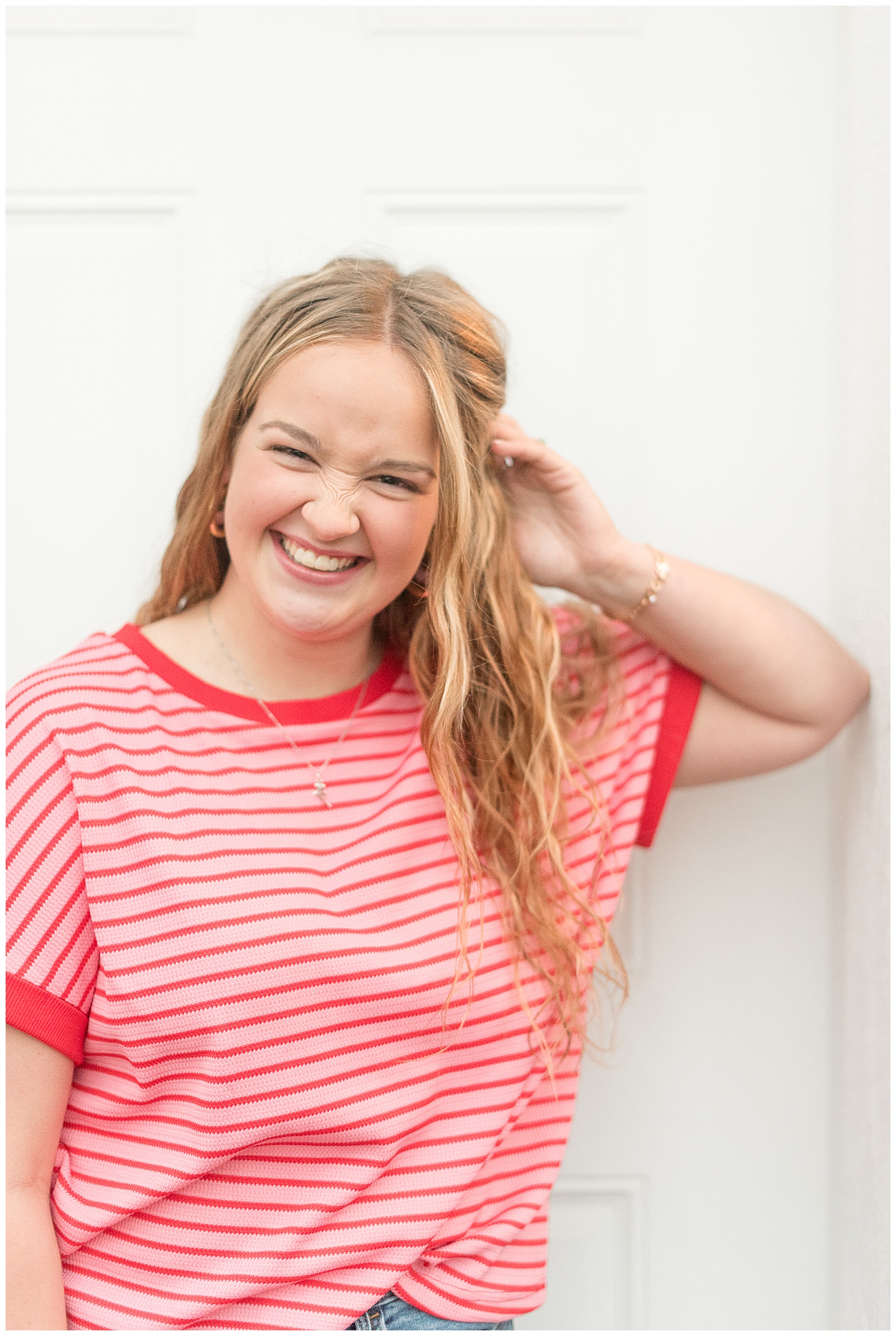 senior girl in red and white striped shirt and blue jeans leaning by white wall for this Stoltzfus Homestead and Gardens Senior Session