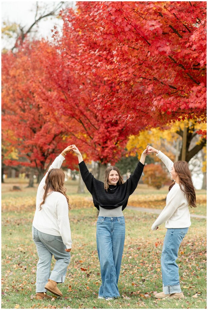 three senior girls twirling around each other by colorful trees for this Fall Senior Team Session in York PA